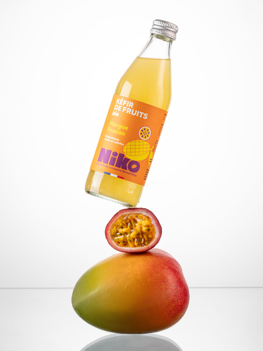 Bouteille de kéfir de fruits mangue passion 33 cl bio Niko en équilibre sur une mangue et un fruit de la passion