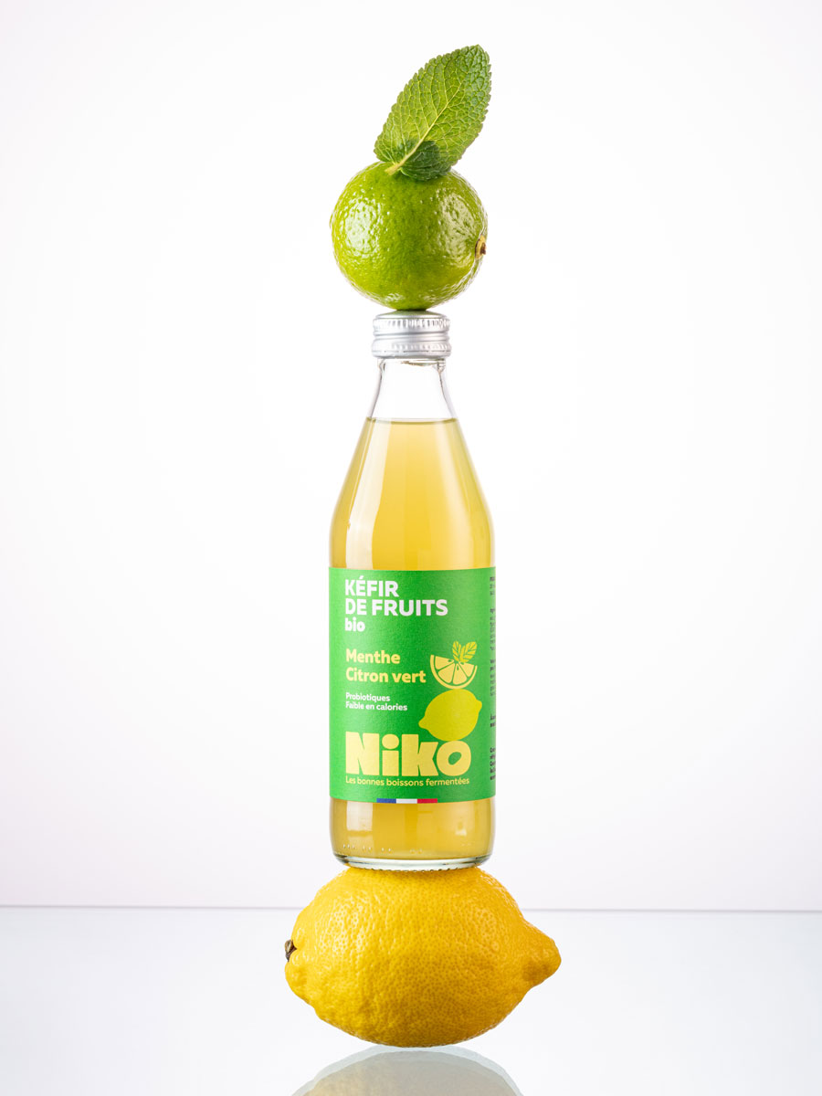 Bouteille de kéfir de fruits menthe citron vert bio Niko en équilibre sur un citron et un citron vert avec feuille de menthe